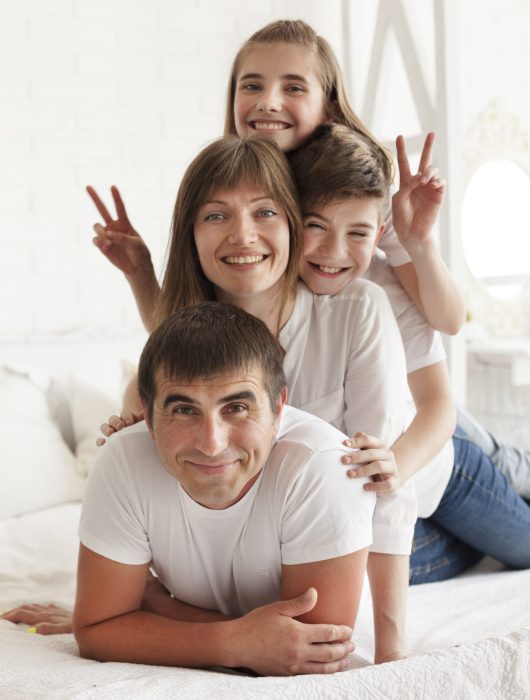 smiling-girl-gesturing-victory-sign-bed-with-her-parent-brother